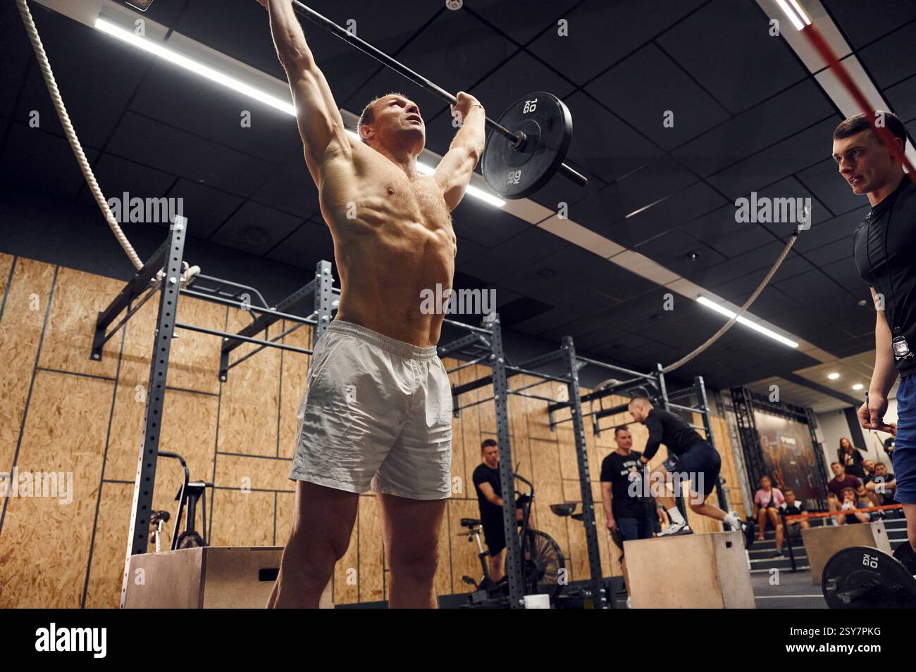 Senza camicia. L'uomo forte sta sollevando il barbell in palestra. Foto Stock