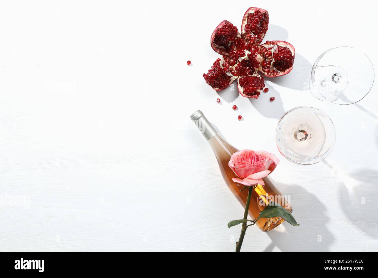 Composizione piatta con delizioso vino rosa e melograno su sfondo bianco. Spazio per il testo Foto Stock