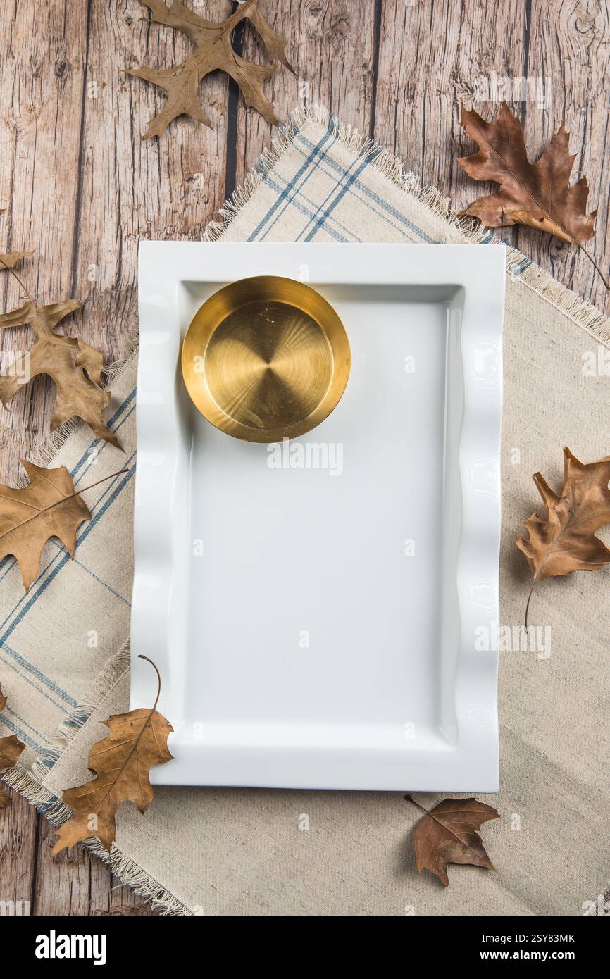 Cena del Ringraziamento. Giorno del Ringraziamento. Foglie autunnali con piatto vuoto bianco, tovagliolo rosso e posate su fondo in legno. Foto Stock