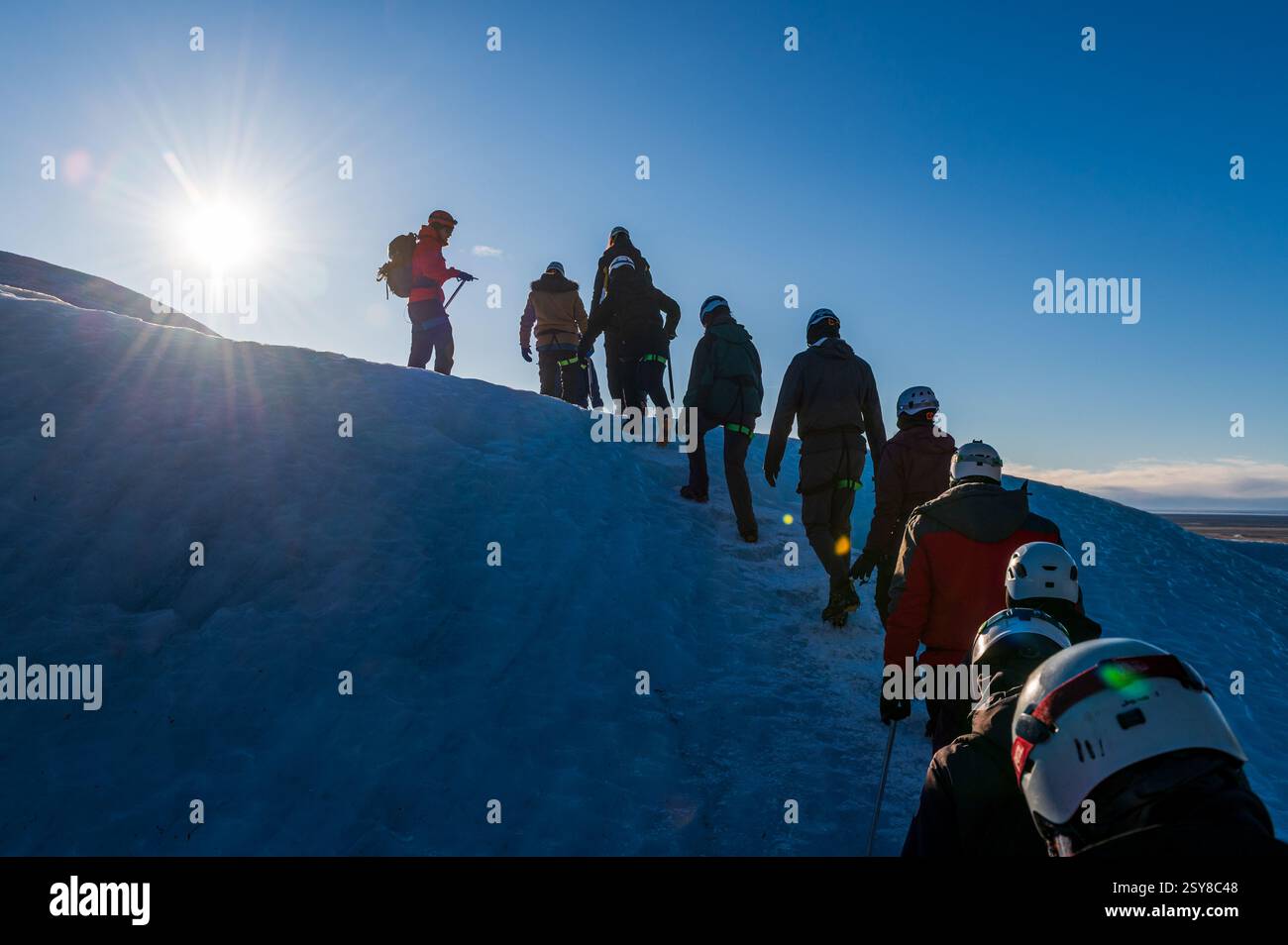 Gruppo di turisti che si allineano tutti insieme per fare un'escursione sul ghiacciaio Vatnajokull in Islanda, un cielo blu brillante Foto Stock