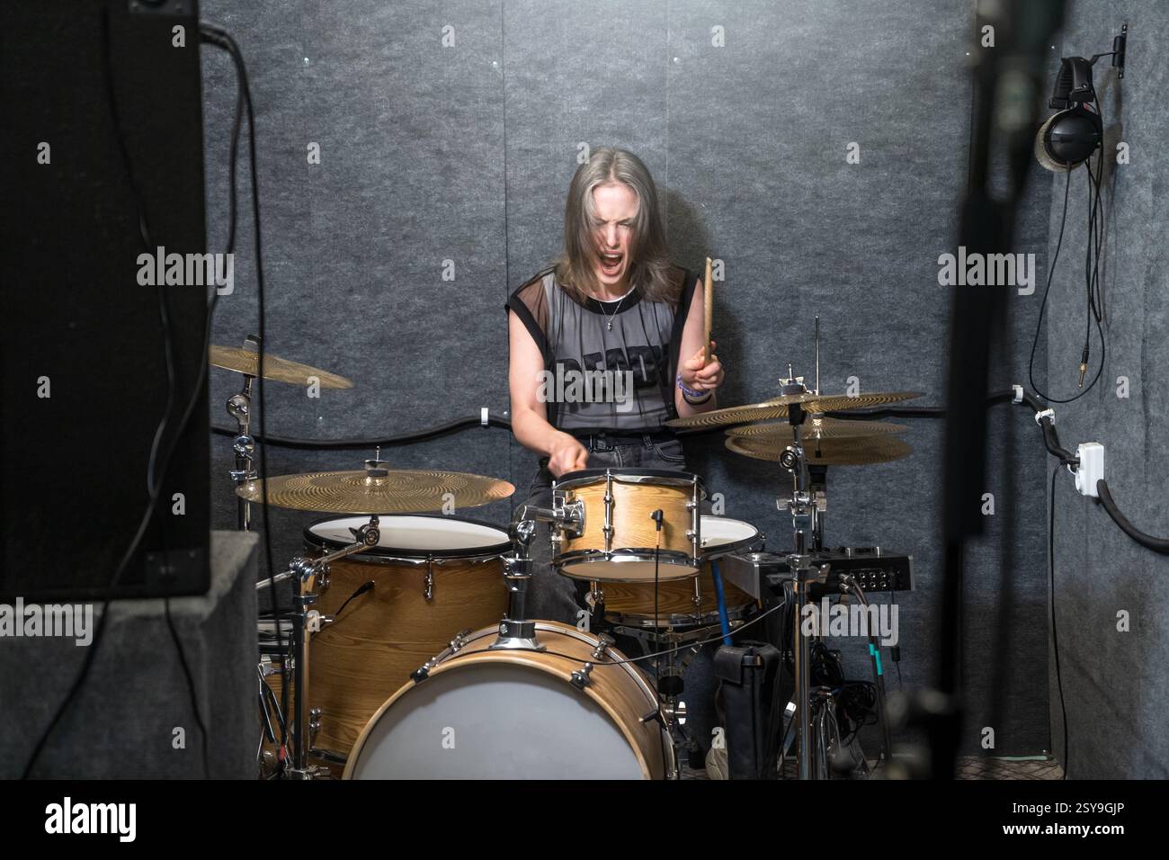 Batterista donna che suona il kit batteria in studio insonorizzato, esprimendo energia e concentrazione. Concetto di musica rock, performance dal vivo, musicisti femminili e percussioni professionali. Foto Stock