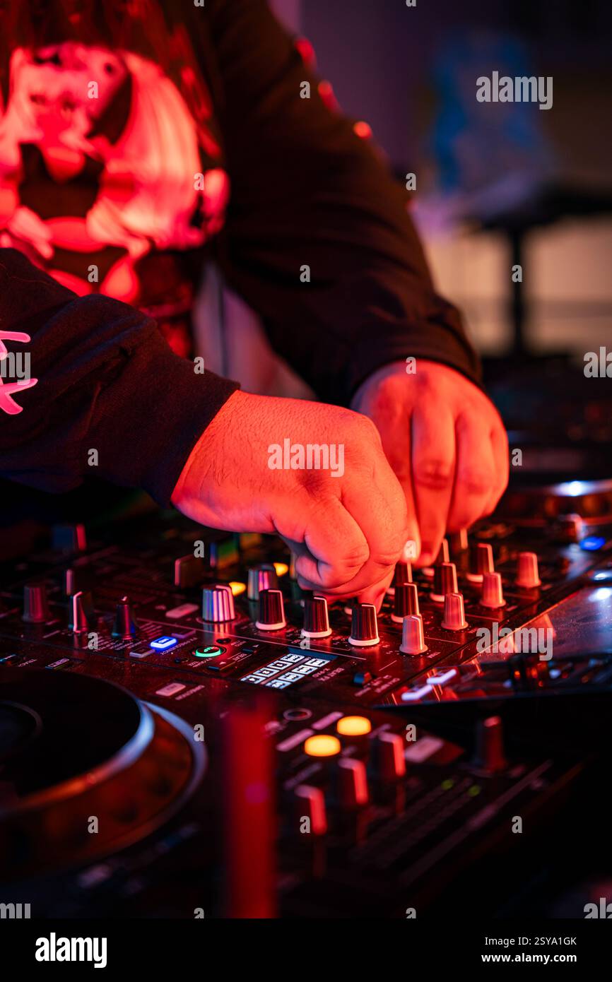 Il DJ mette le mani su un mixer, entrambe le mani sono sul tabellone e l'ambiente è illuminato da luci rosse Foto Stock