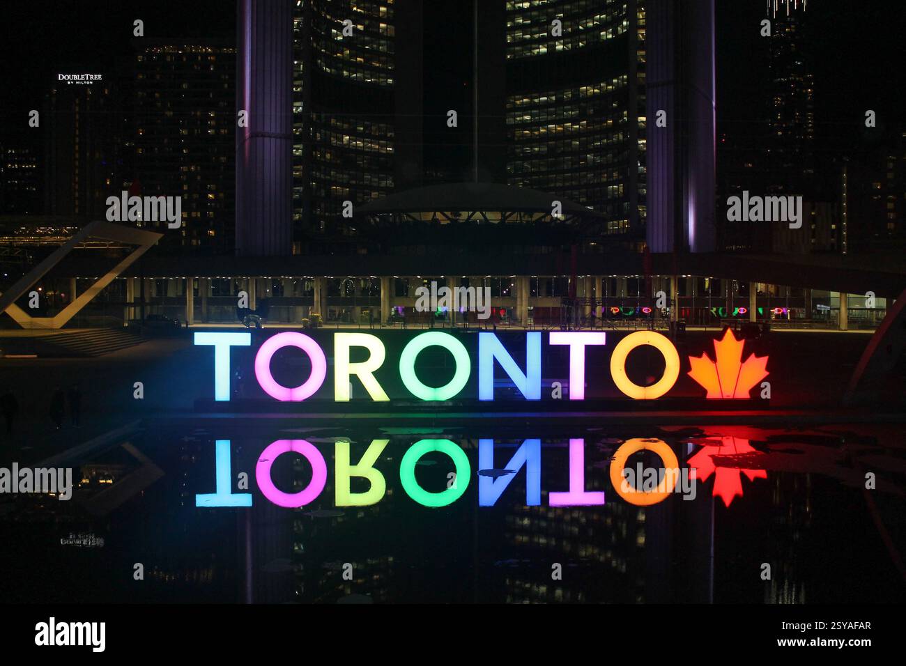 Colorato cartello Toronto illuminato in Nathan Phillips Square di notte con illuminazione arcobaleno, icona della foglia d'acero e riflessi sull'acqua Foto Stock