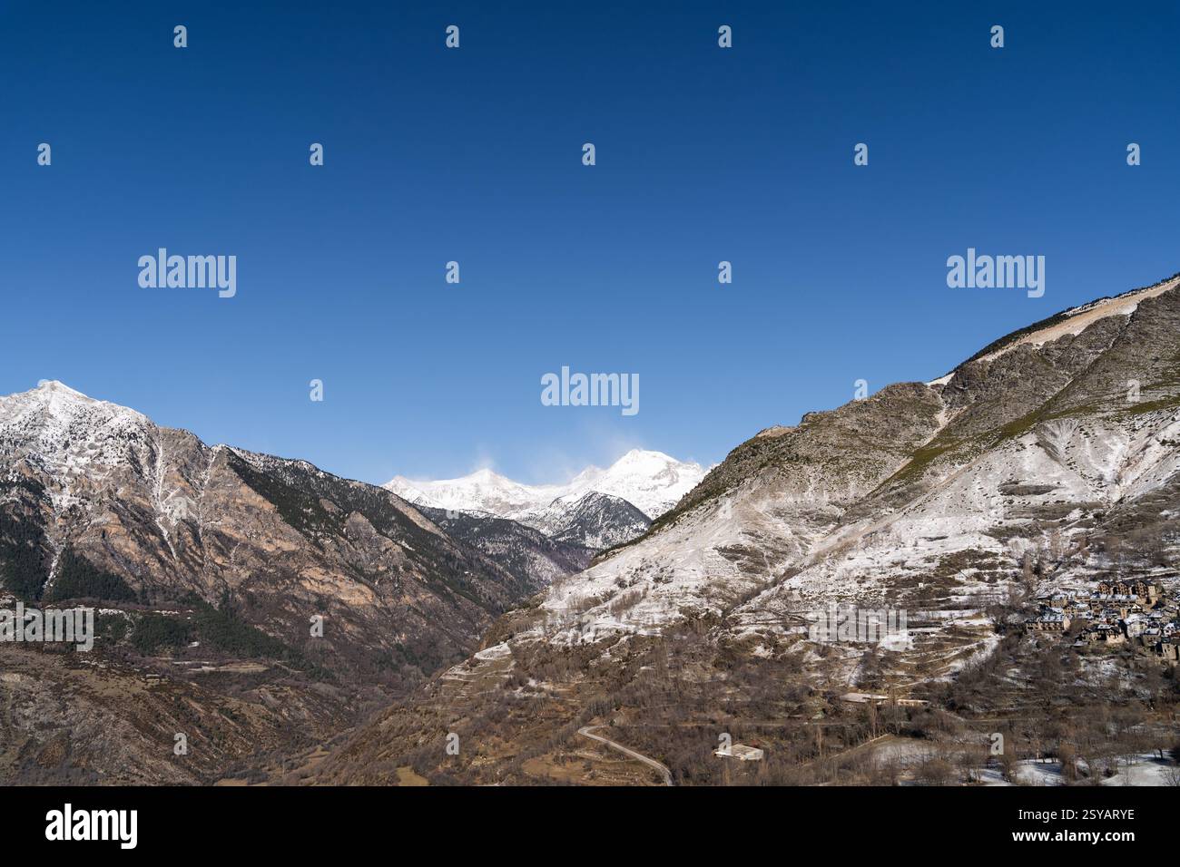 Un paesaggio rurale mozzafiato caratterizzato da maestose montagne innevate sotto un cielo azzurro, con un piccolo villaggio annidato sulle piste. Foto Stock