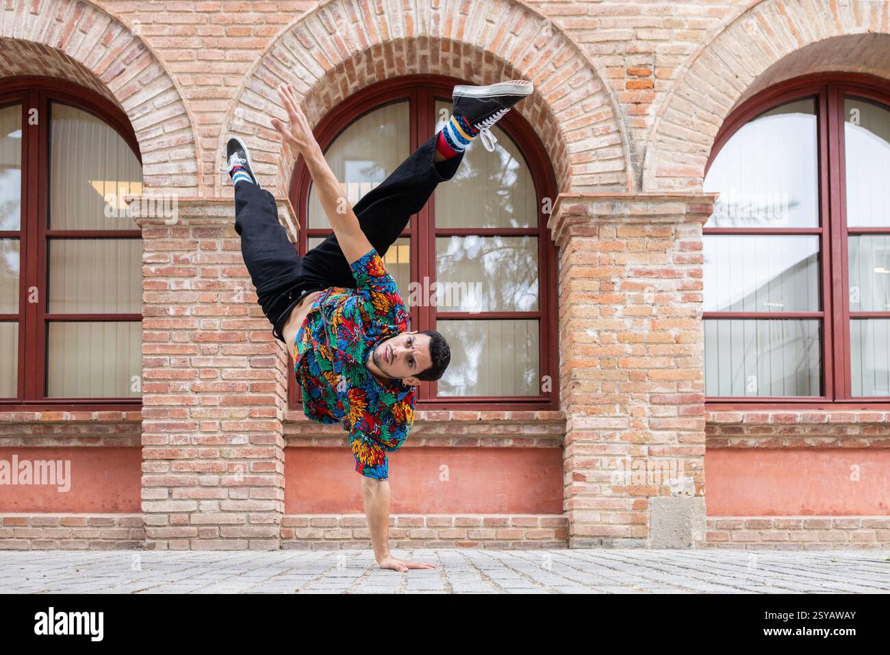 Una vibrante ballerina cubana esegue un'asta dinamica su uno sfondo di pareti in mattoni. Il suo abbigliamento colorato e il suo movimento espressivo catturano l'energia di S. Foto Stock
