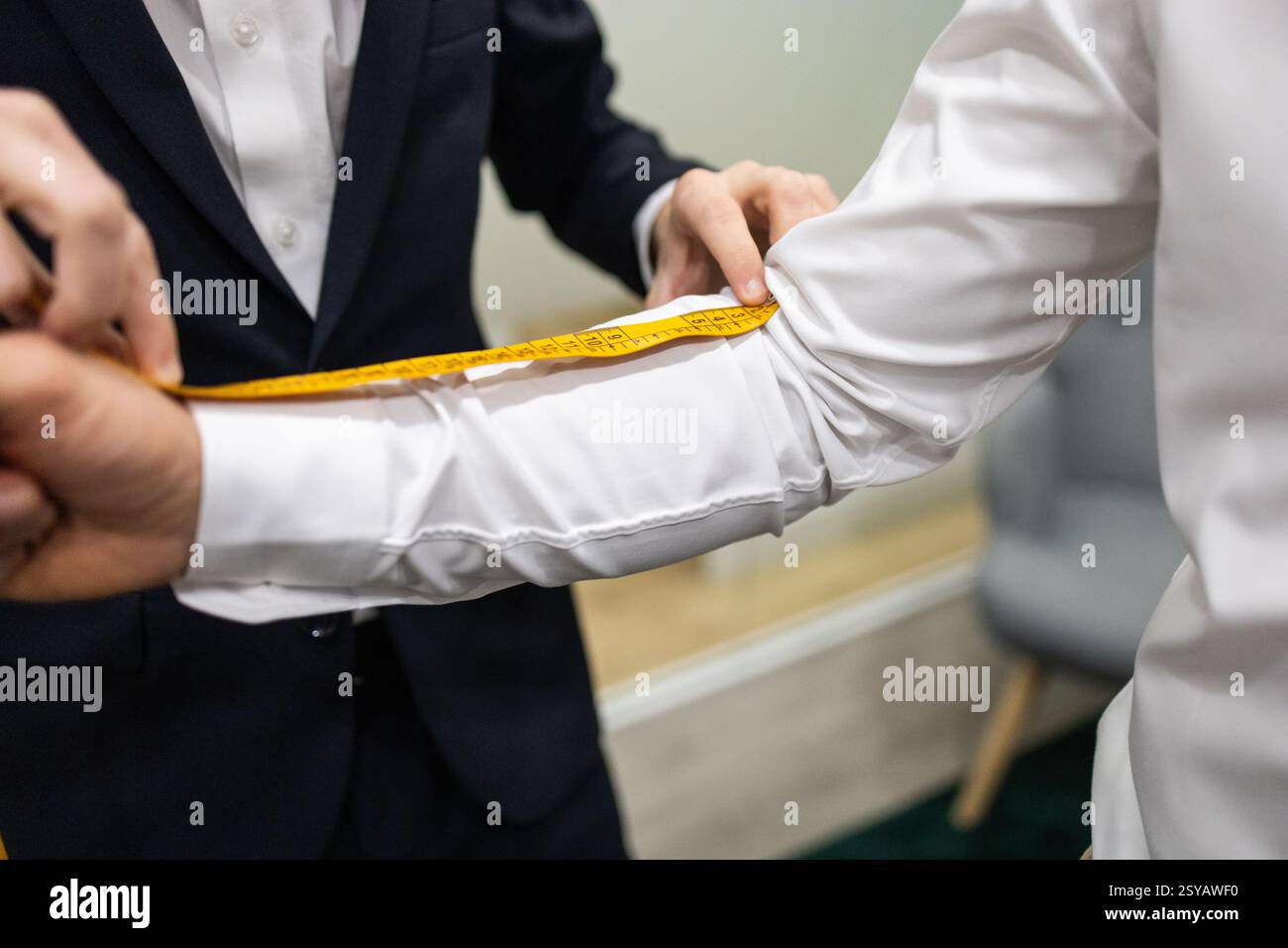 Primo piano di un sarto che misura il braccio di un cliente con un nastro di misurazione giallo in un negozio di abiti. La scena cattura la precisione essenziale per crea Foto Stock