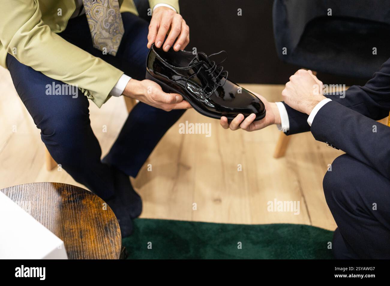 L'uomo in un negozio di abiti valuta una scarpa in pelle nera elegante. L'impostazione ha un tappeto verde che indica un ambiente professionale. Foto Stock