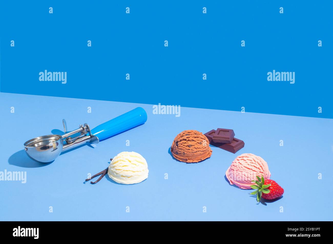 Vivace esposizione di palline di cioccolato, vaniglia e gelato alle fragole con barrette di cioccolato e fragole fresche su uno sfondo blu a due tonalità. Foto Stock