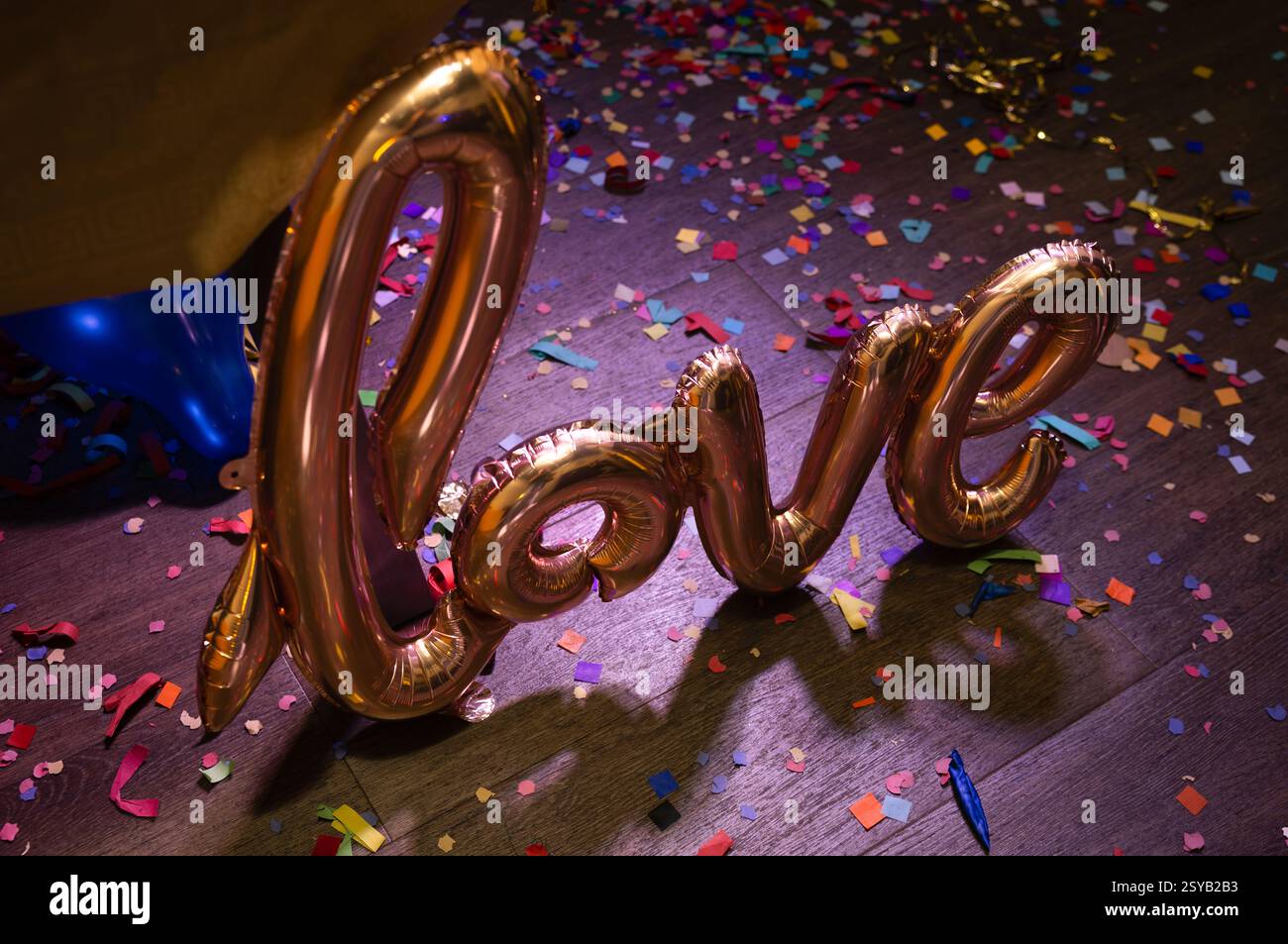 Un palloncino in lamina dorata che scrive "amore" su un pavimento in legno ricoperto di coriandoli colorati, creando un'atmosfera festosa e romantica perfetta per i festeggiamenti Foto Stock