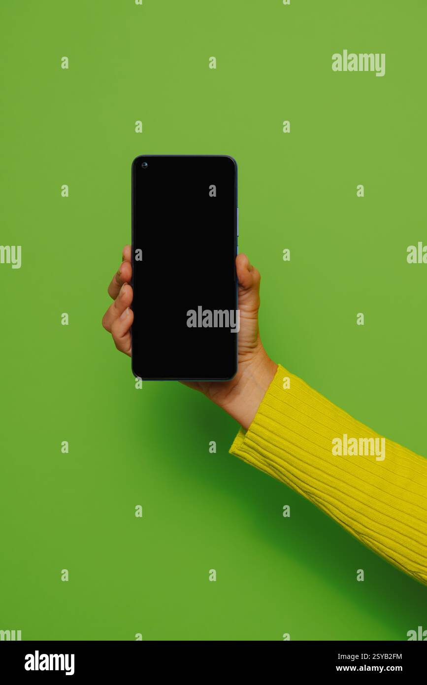Ritaglia la mano di una persona anonima che regge lo smartphone con schermo nero su sfondo verde Foto Stock