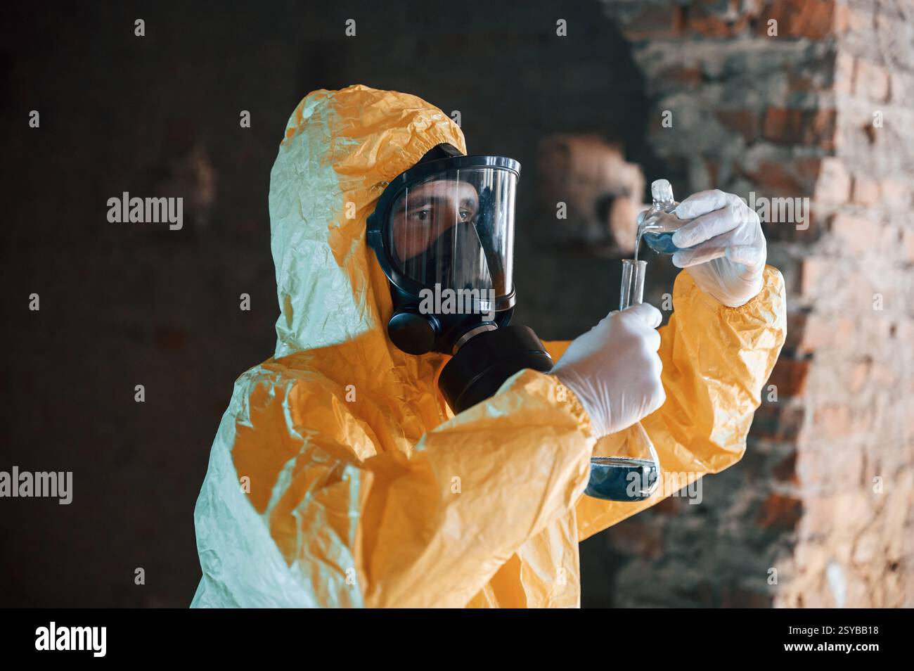 Una provetta con materiali radioattivi. Uomo vestito con una tuta di protezione chimica tra le rovine dell'edificio post apocalittico. Foto Stock