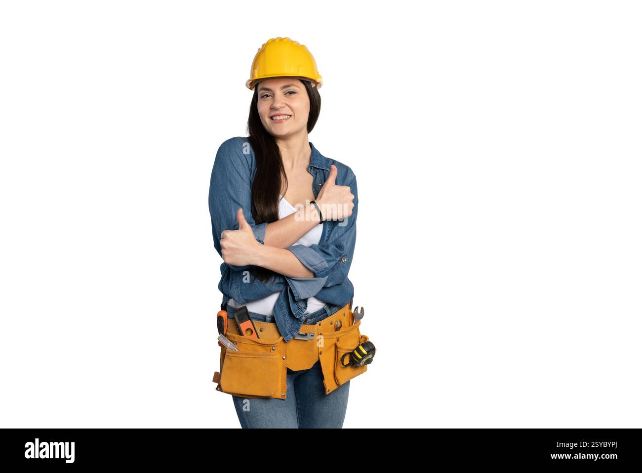 Una lavoratrice edile sorridente con una camicia in denim, una canotta bianca e una cintura portautensili ti regala un tocco di sicurezza quando si incrocia le braccia. Indossa un Foto Stock