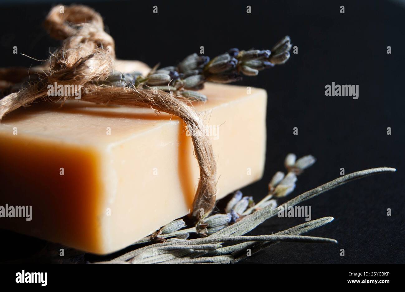 Una delicata saponetta di lavanda con fiocco rustico decorativo, su uno sfondo blu scuro, ideale per temi di benessere e cura personale. Foto Stock