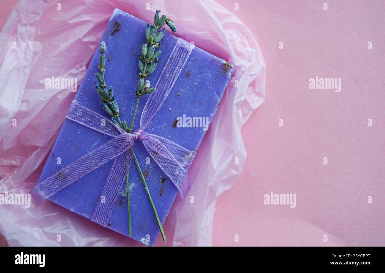 Sapone viola lavanda realizzato a mano elegantemente avvolto da un fiocco decorativo, posizionato su un morbido sfondo rosa. Foto Stock