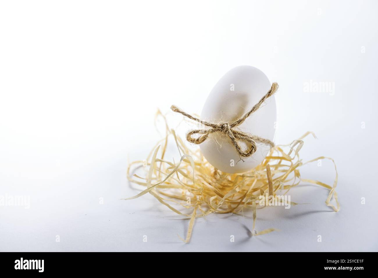 Uovo di pollo bianco decorato in stile minimalista per Pasqua con un arco di filo naturale rustico su lana di legno, sfondo grigio chiaro con spazio per le copie, sele Foto Stock