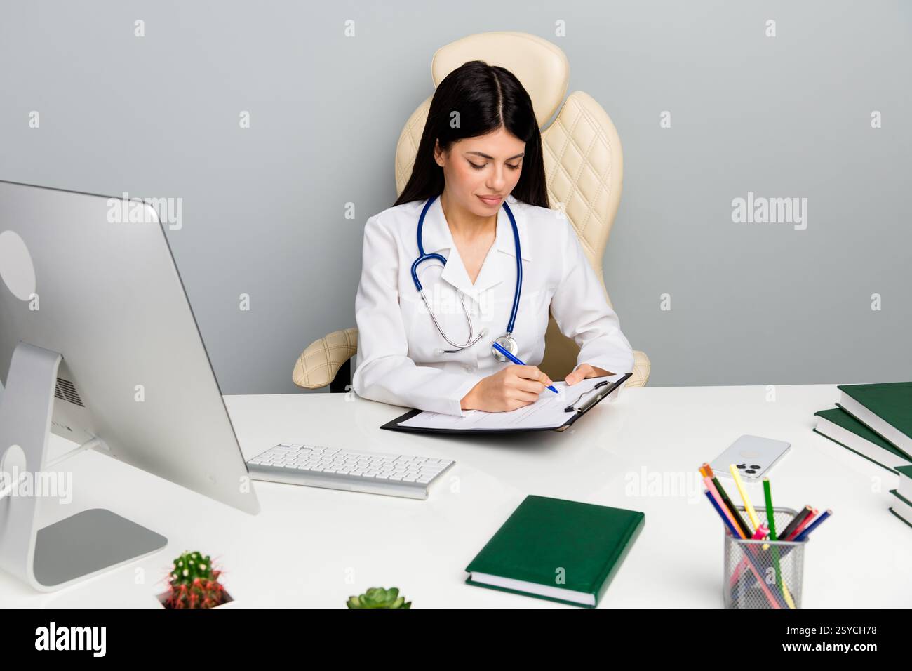 Professionista sanitario in camice bianco che esamina documenti da una scrivania moderna in ambiente clinico Foto Stock