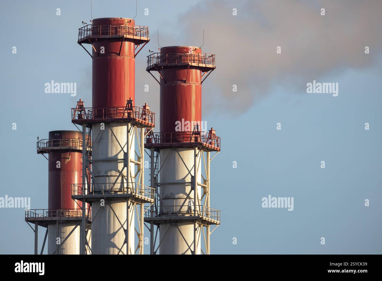 Pile di fumo rosse e bianche che rilasciano emissioni nell'aria, mostrando un impianto industriale contro un cielo azzurro a contrasto. Adatto per topi Foto Stock
