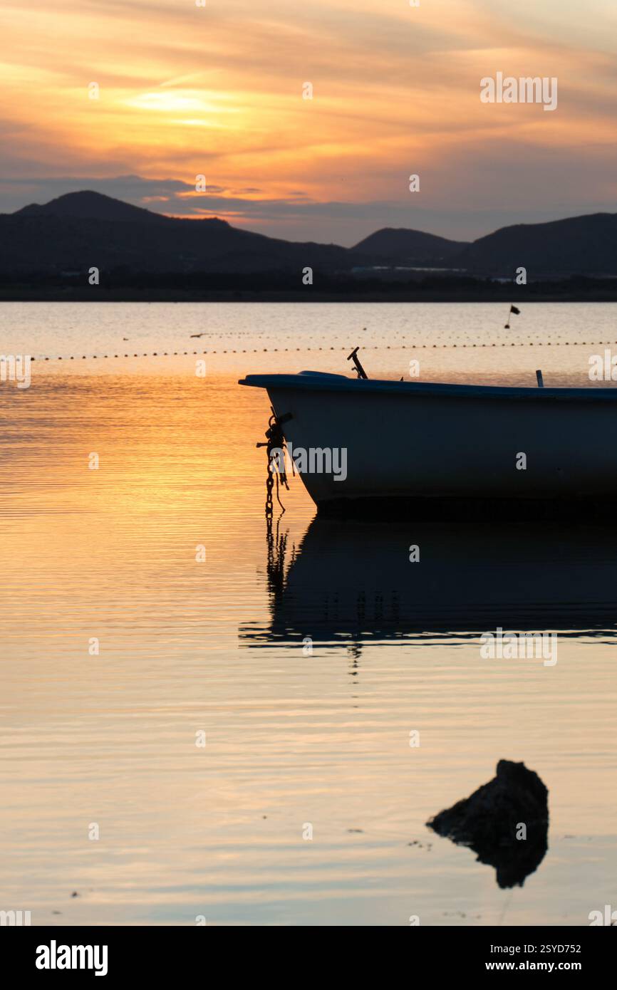 Barca ancorata al tramonto a Playa Honda, la Manga del Mar Menor, Cartagena, regione di Murcia, Spagna, con acque calme e cielo arancione riflesso Foto Stock