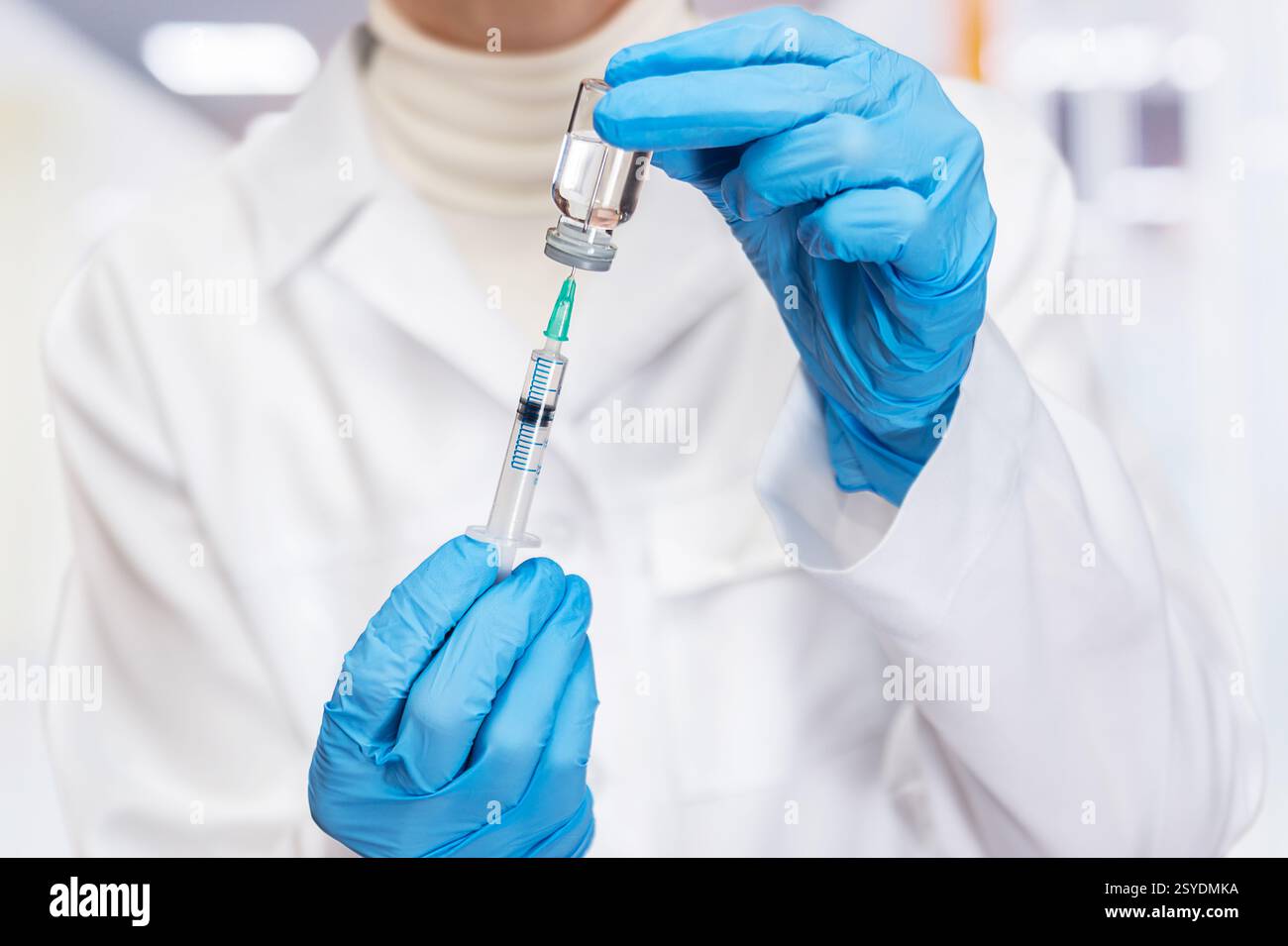 Un operatore sanitario qualificato in guanti sta aspirando il liquido vaccino in una siringa in una clinica ben illuminata. Foto Stock