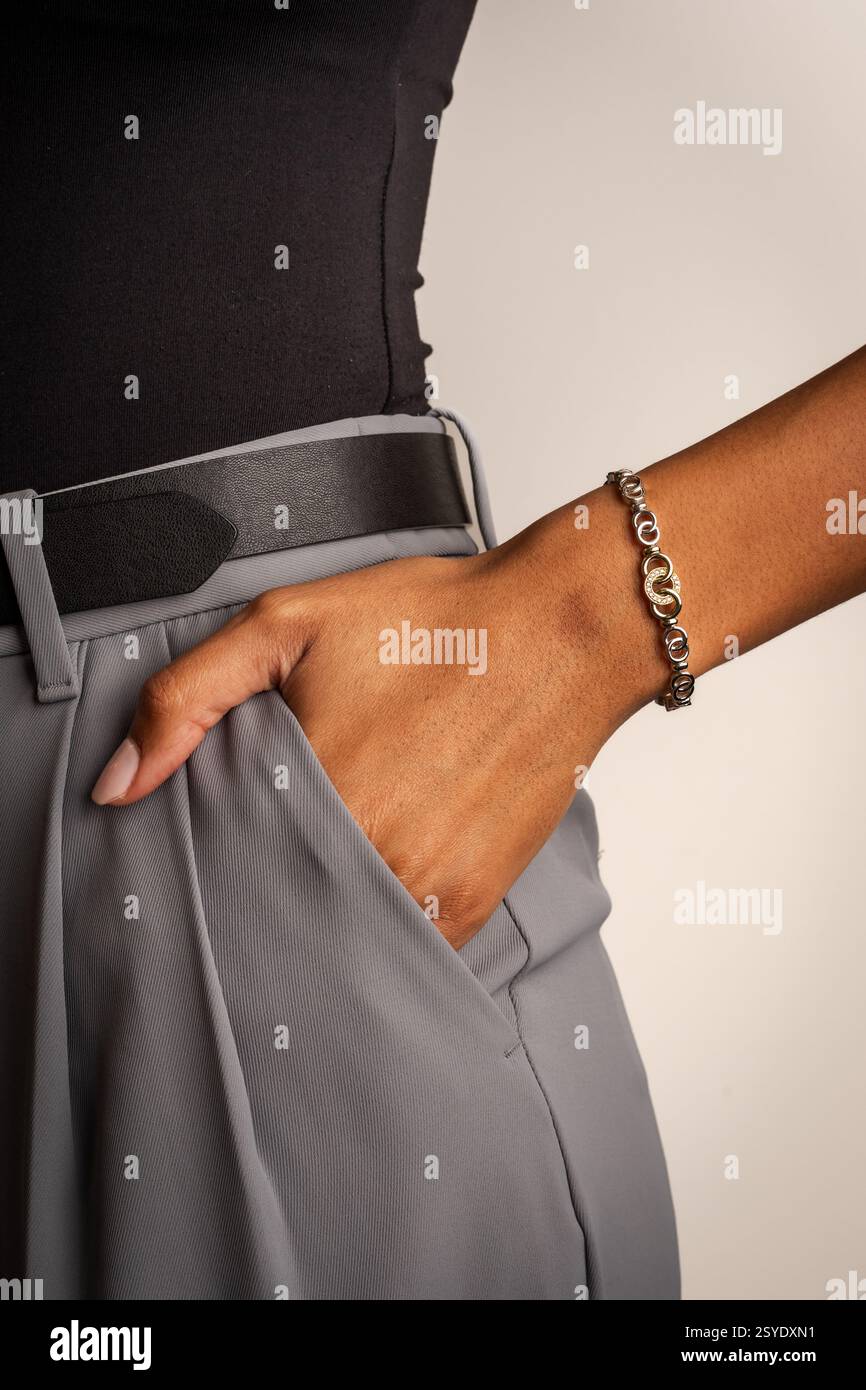 Persona che indossa una parte superiore nera e pantaloni grigi con cintura in pelle e un bracciale con catena dorata sul polso. Foto Stock