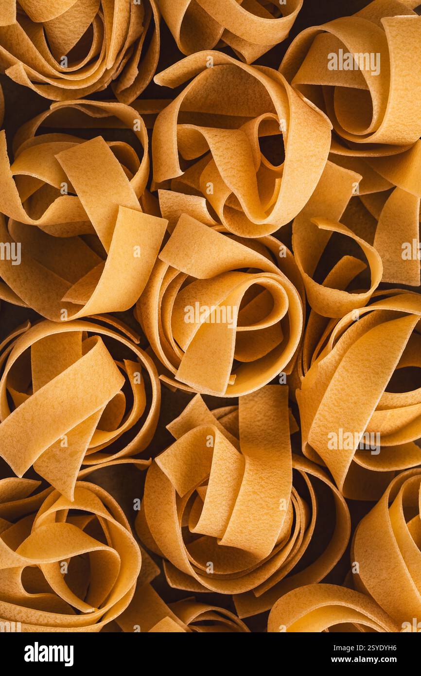 Primo piano di nidi di pappardelle secche che che mostrano gli ampi nastri dorati piatti disposti in formazioni ondulate. Foto Stock