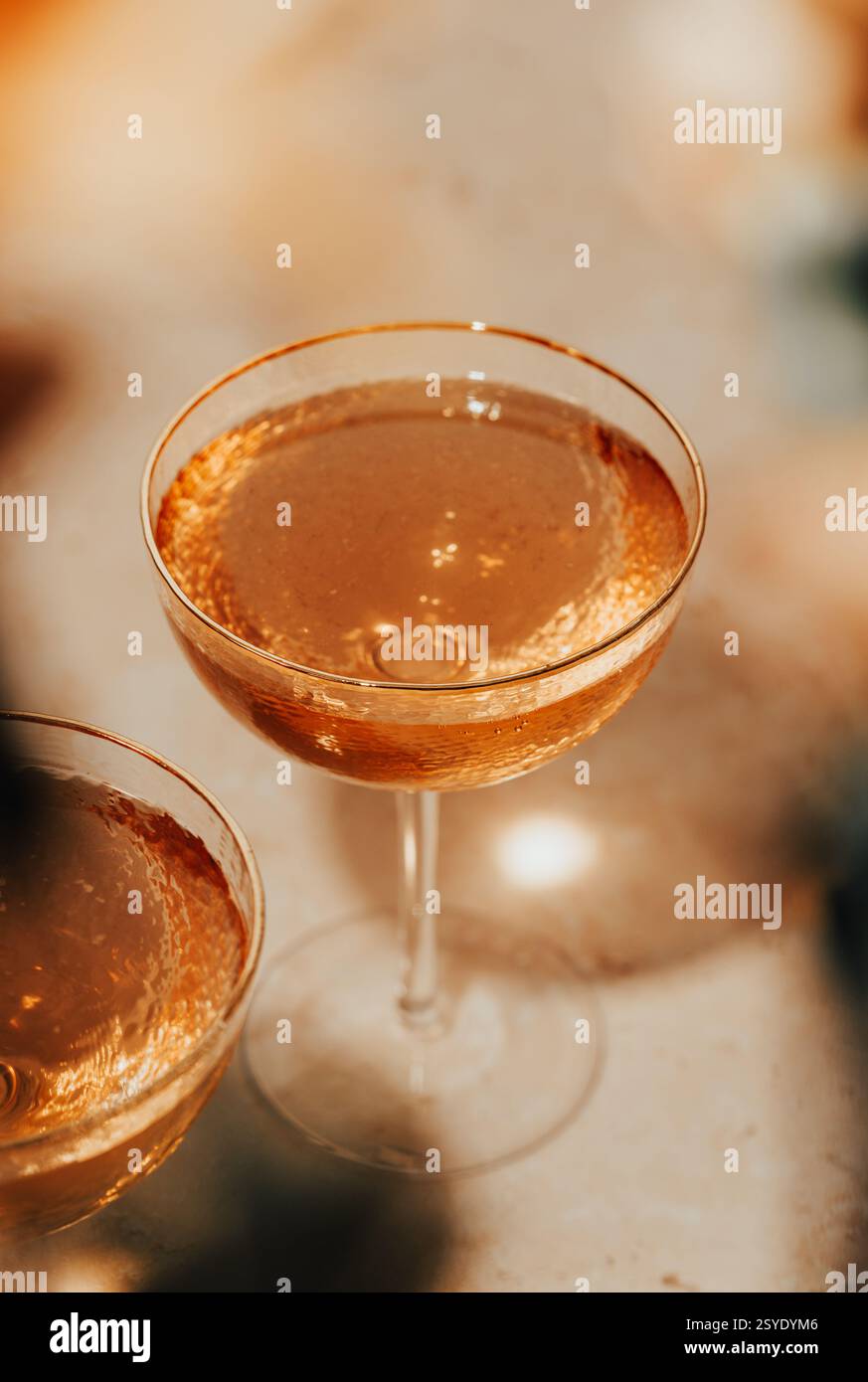 Un cocktail dorato frizzante in un bicchiere coupé testurizzato, illuminato da una luce calda, perfetto per una festa o un brindisi d'oro. Foto Stock