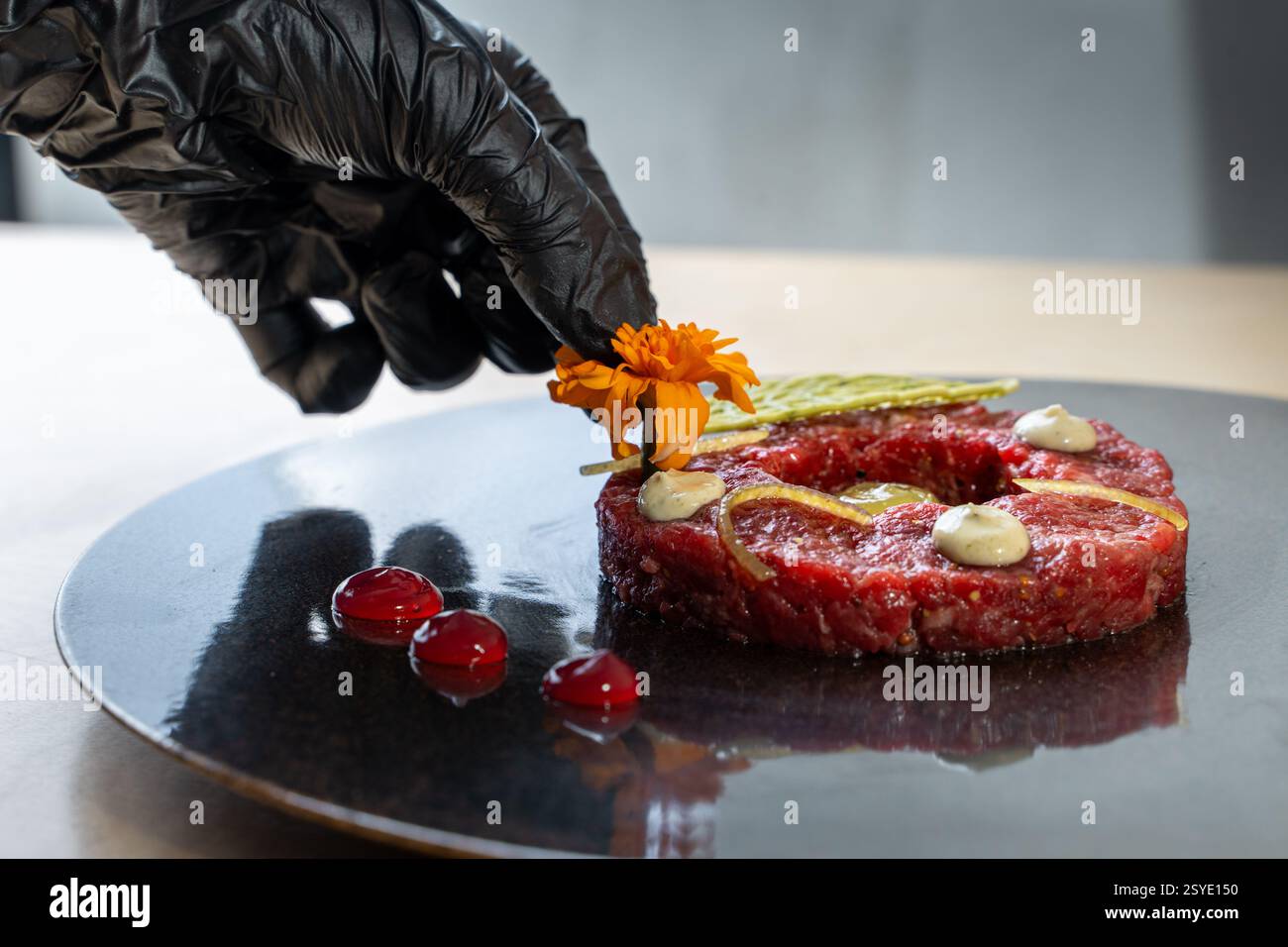 Uno chef professionista guarnisce con cura una tartare di manzo gourmet con fiori commestibili e dettagli raffinati in un ristorante di alto livello che mette in mostra arti culinarie Foto Stock