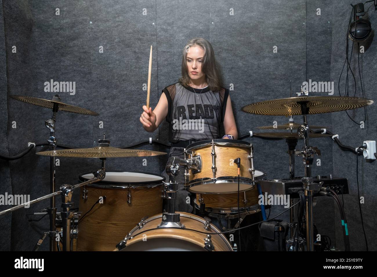 Batterista donna che suona la batteria in studio insonorizzato. Musicista concentrato che tiene in mano le bacchette di batteria e si esibisce in un ritmo energico. Prove musicali professionali e sessioni di pratica. Foto Stock