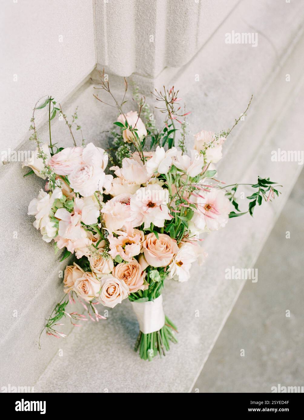 Un bouquet pastello di rose e fiori selvatici è splendidamente disposto su una superficie di pietra, che mostra colori delicati. Foto Stock