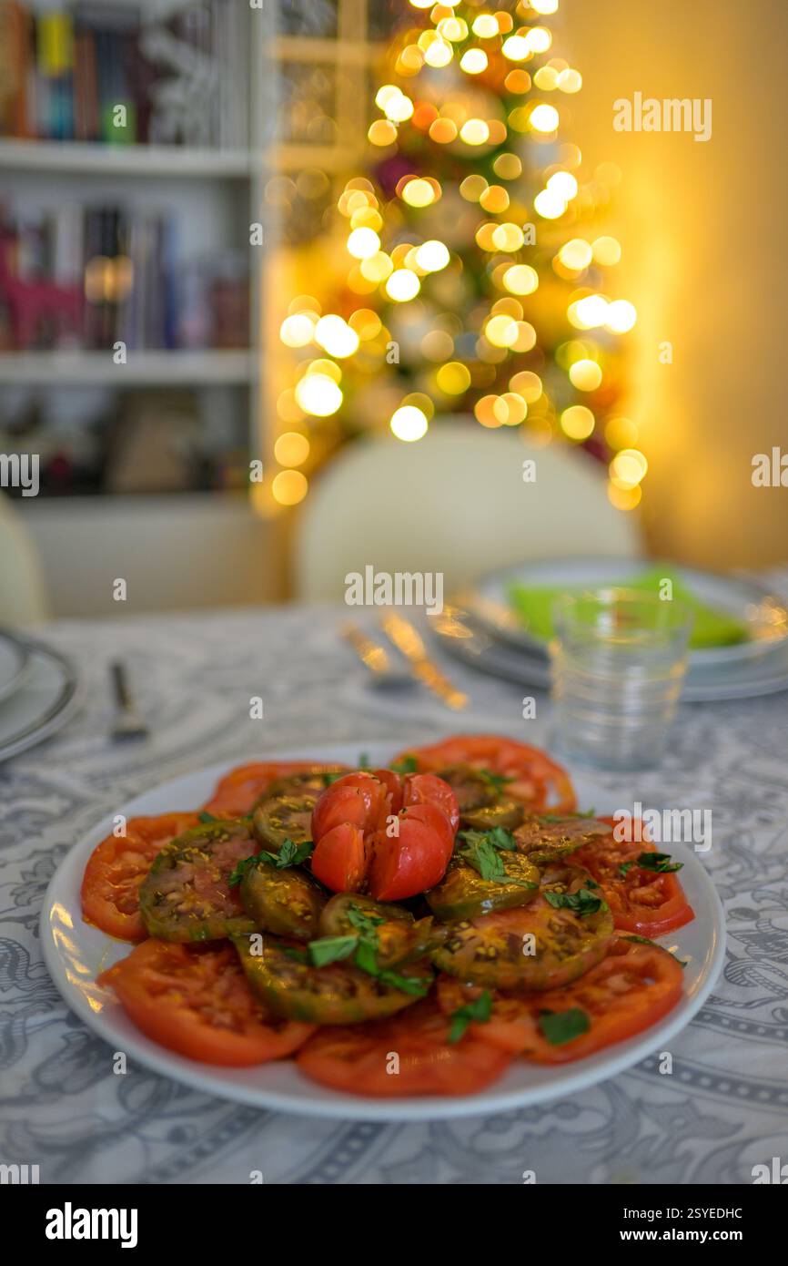 Un tavolo splendidamente organizzato per un pasto di Natale presenta piatti vivaci e accenti decorativi tra luci soffuse e luminose. Foto Stock