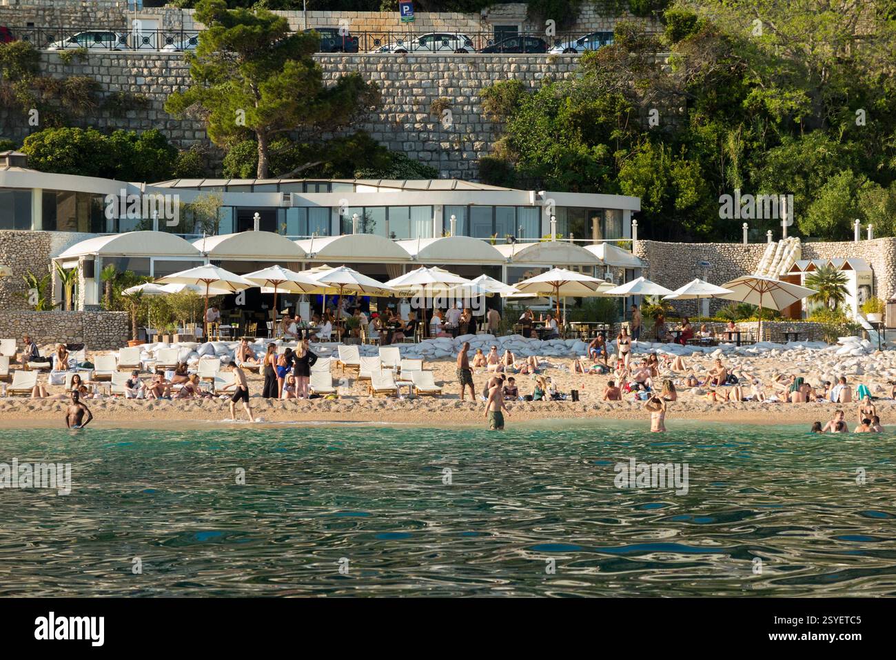 Banje Beach & turisti, con il Banje Restaurant Cafe. La spiaggia si trova di fronte alla porta di Ploče, l'ingresso orientale della città Vecchia. Dubrovnik. Croazia. (138) Foto Stock