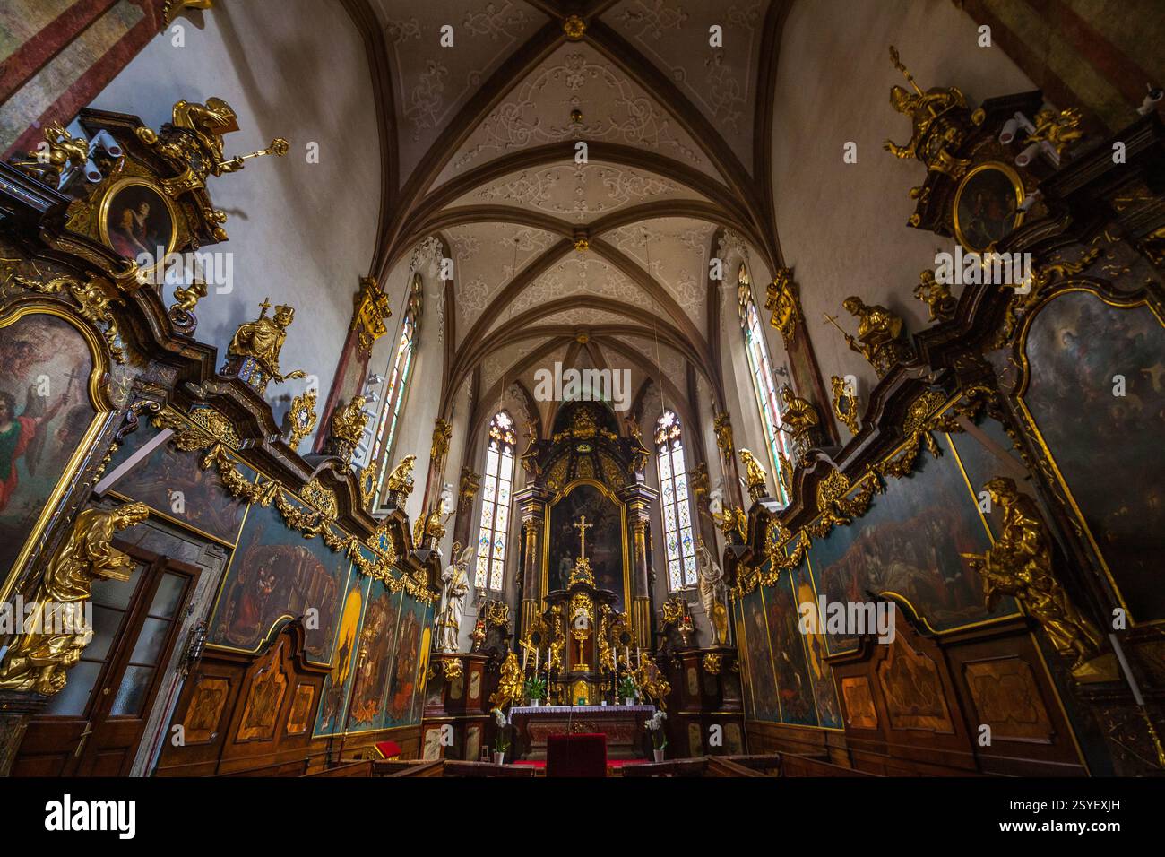 Vista interna di una chiesa con un alto soffitto a navata con volte ad arco, decorazioni dorate ornamentali e un altare centrale, visto da un po' Foto Stock