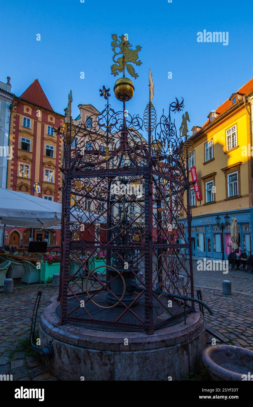 Una fontana decorativa con una statua di leone dorato sulla sommità, circondata da un recinto in metallo ornato, si erge in una piazza di ciottoli con bolla colorata Foto Stock