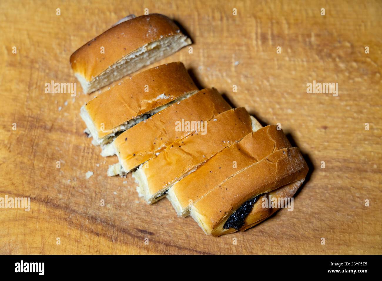 Il pane appena sfornato viene tagliato a fette uniformi, rivelando un ripieno scuro all'interno. Il pane poggia su un tagliere di legno, che ne mostra la consistenza e il co Foto Stock