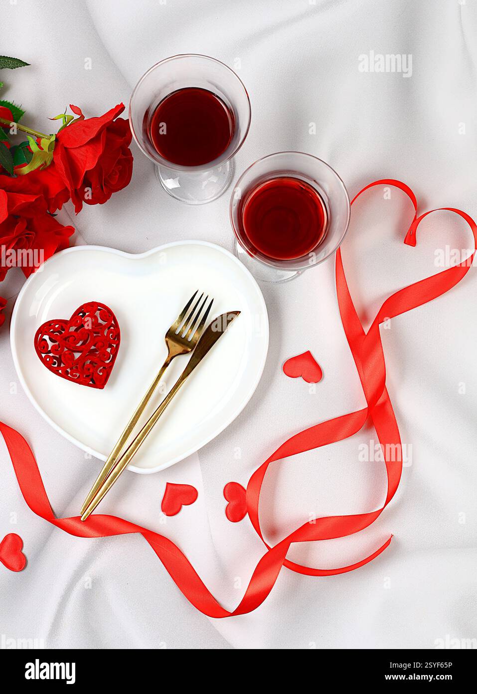 Tavolo festivo, disposizione del menu per San Valentino, posate con cuore su piatto e bicchieri con vino, composizione festosa con bouquet di Foto Stock