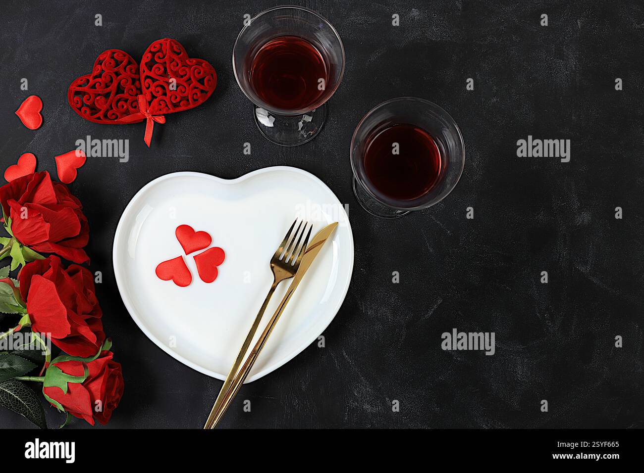 Tavolo festivo, menu' disegnato per San Valentino, posate con cuore su piatto e bicchieri con vino rosso, composizione festosa con bouquet Foto Stock