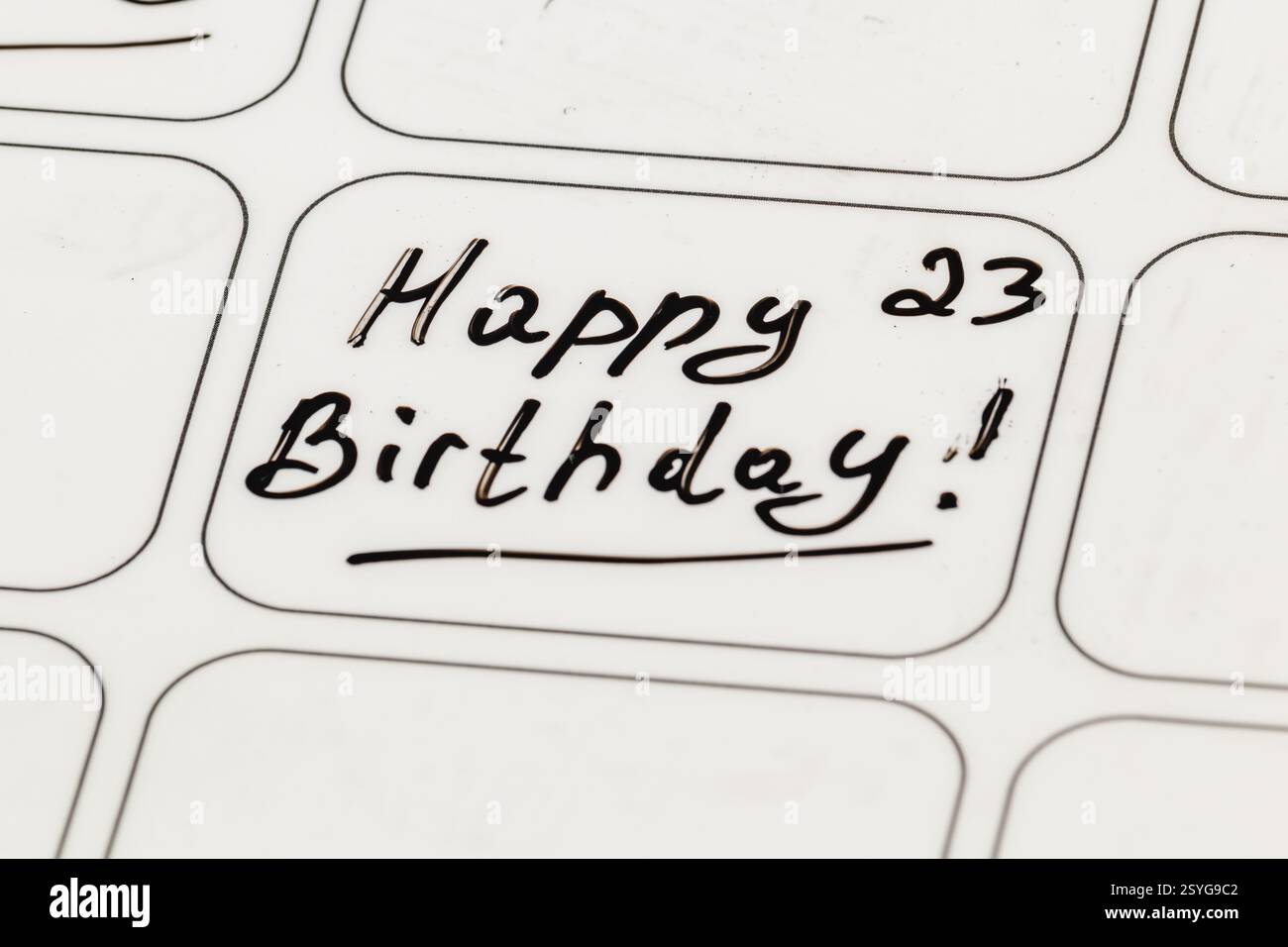 Una nota scritta a mano che augura un felice ventitreesimo compleanno è esposta su una superficie bianca. Il messaggio presenta una scritta divertente e cursiva, che aggiunge un tocco personale a Foto Stock