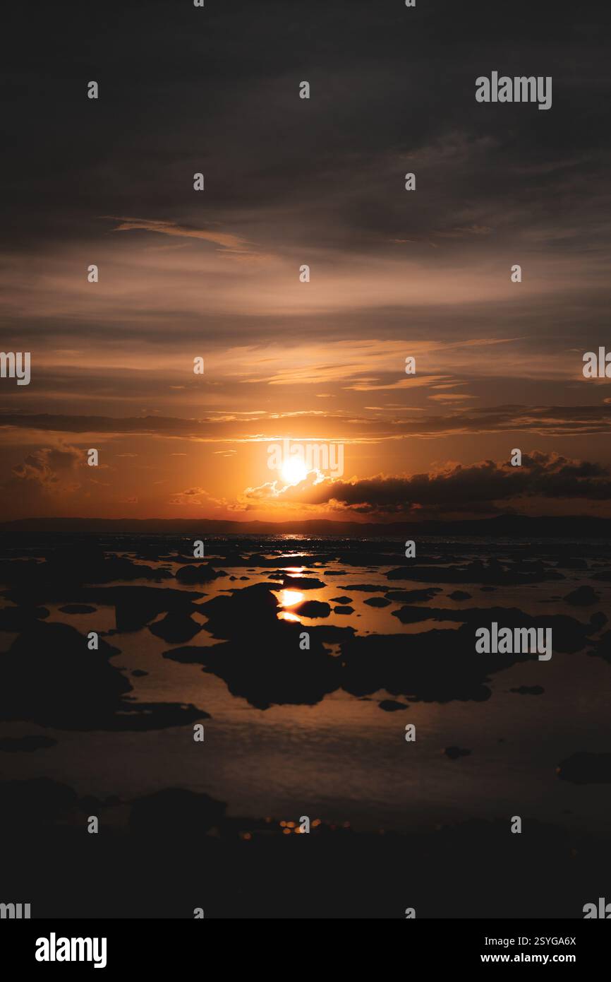 Mentre il sole bacia l'orizzonte, il cielo si mette a fuoco, sussurrando addio in tonalità d'oro, rosa e viola. Foto Stock