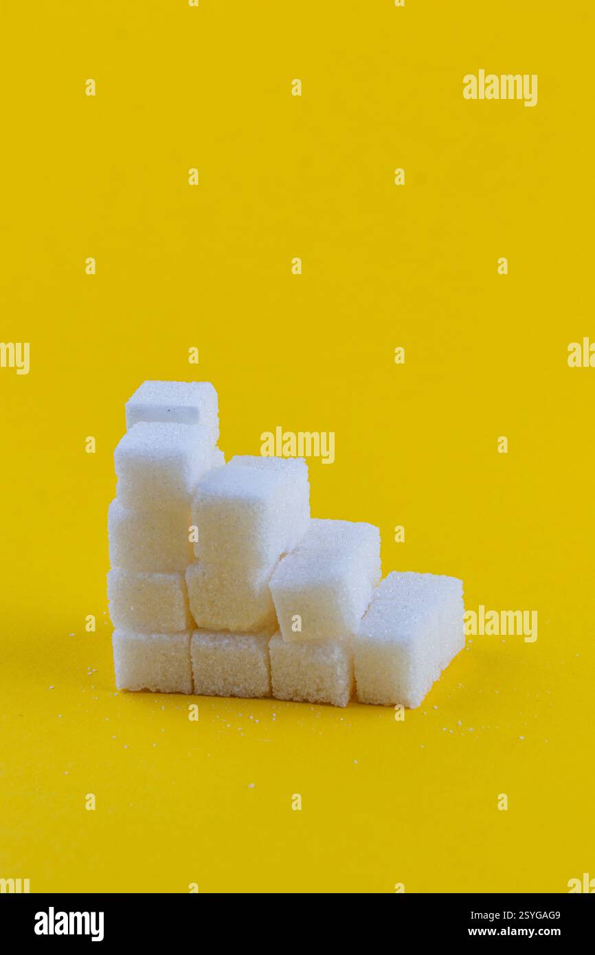 I cubetti di zucchero sono accuratamente impilati in una formazione a gradini su uno sfondo giallo vibrante, creando un effetto visivo divertente e creativo che disegna Foto Stock