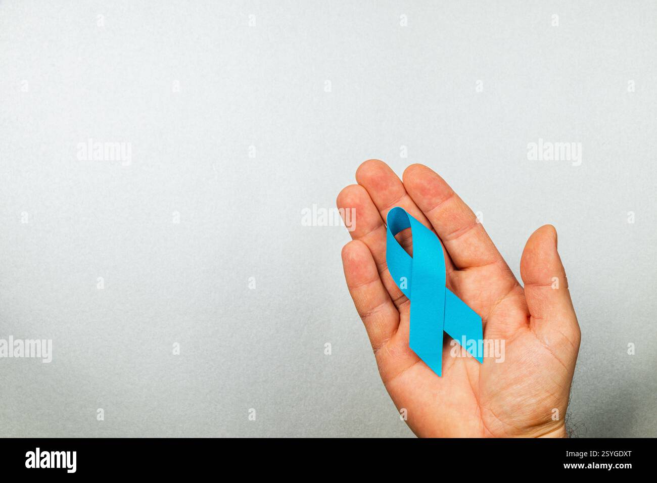Una mano maschile mostra un nastro blu di consapevolezza, che rappresenta il supporto per l'individuazione e il trattamento del cancro. Questo aspetto sottolinea l'importanza delle unders Foto Stock