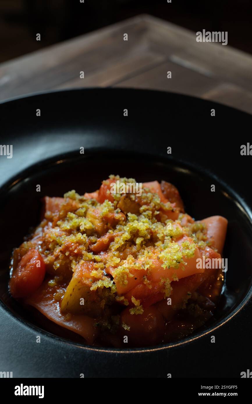 Un primo piano di pasta paccheri gourmet servita con un ricco sugo di pomodoro, verdure arrostite e un condimento di croccanti pangrattati, presentati elegantemente Foto Stock