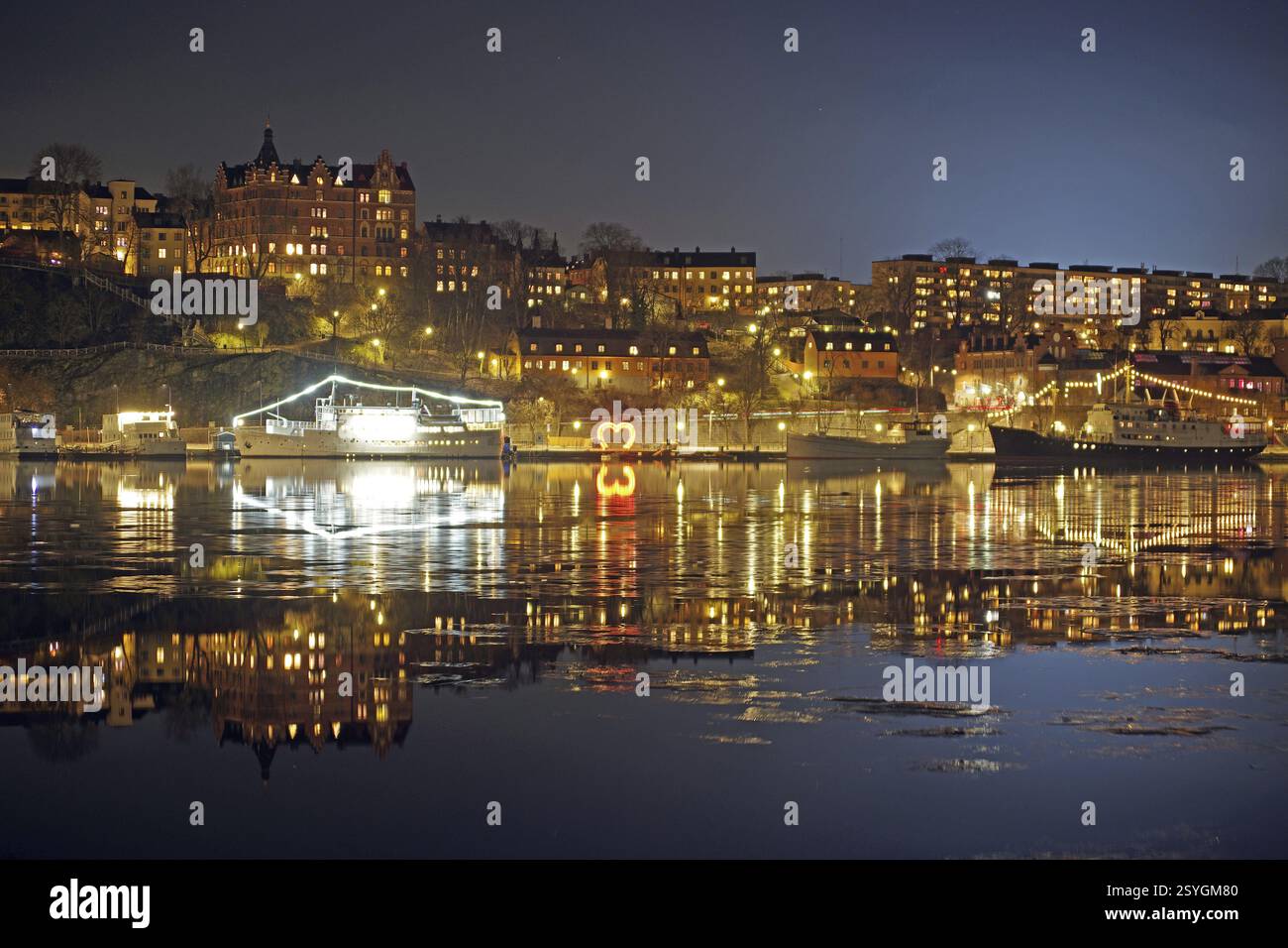 Vista notturna della città con edifici illuminati e riflessi sull'acqua, inverno, ghiaccio, capitale, Soedermalm, Stoccolma, Svezia, Europa Foto Stock