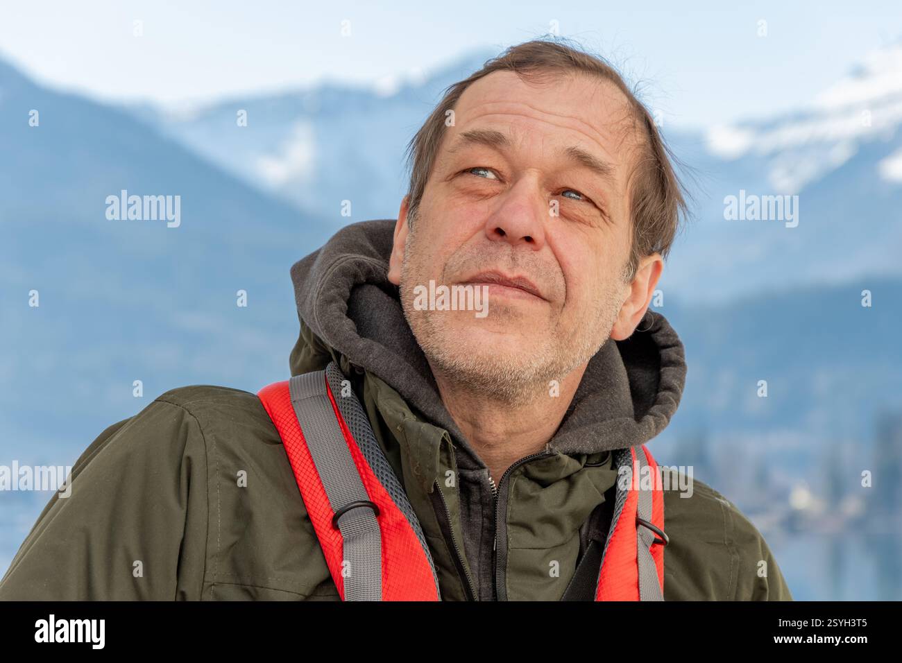 Un viaggiatore con uno zaino si erge davanti a vette innevate e a un lago riflettente Foto Stock