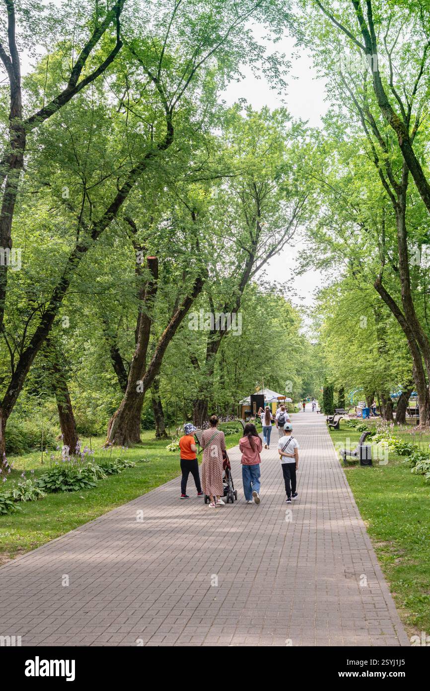 Parco cittadino in una giornata estiva, prati verdi con erba e alberi, gente che cammina. Foto Stock