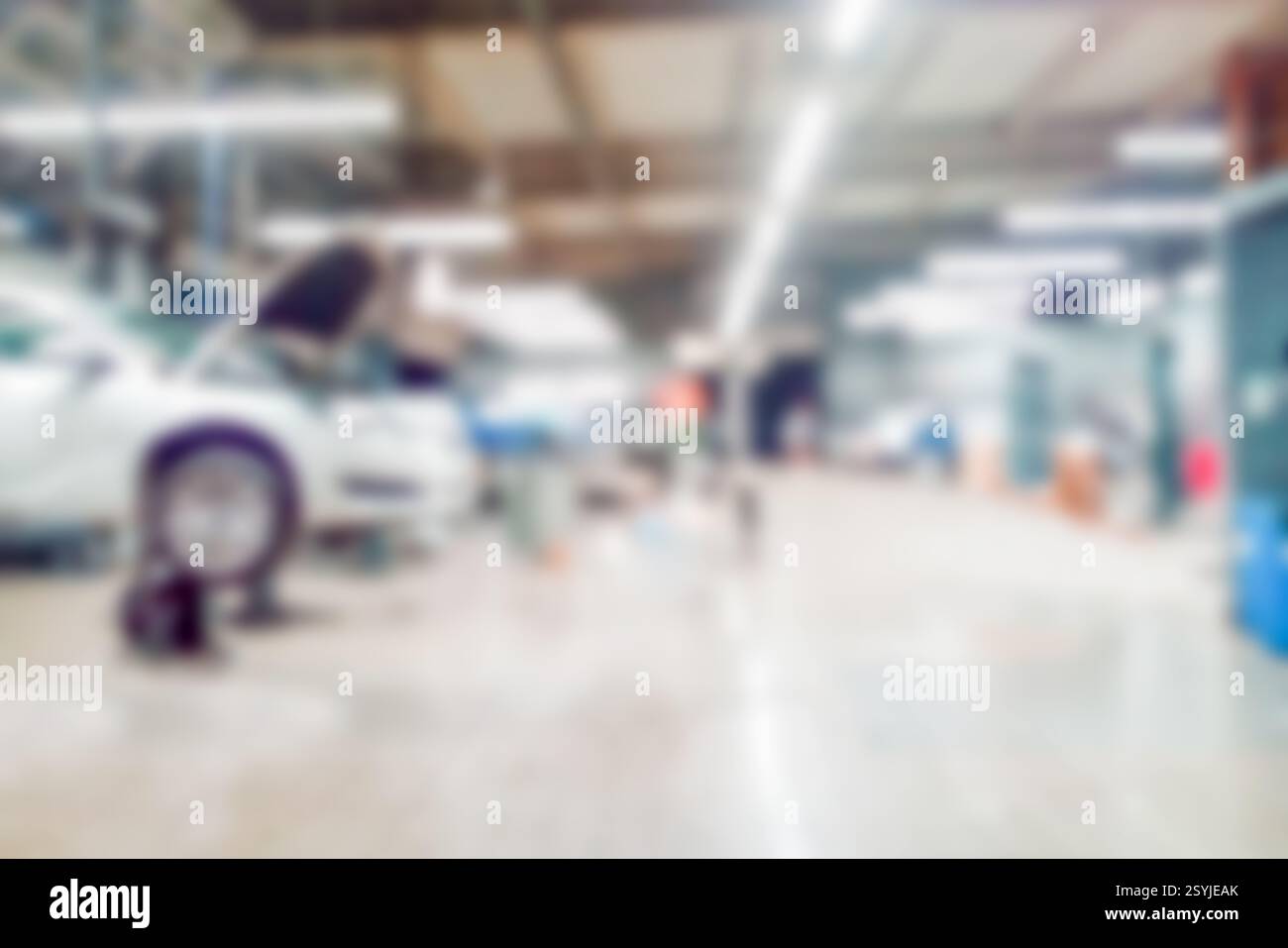 Stazione di servizio di riparazione con vetture moderne sollevate in fase di manutenzione e tecnici su sfondo sfocato con molte lampade a diodi. Servizio auto, tecnologia Foto Stock