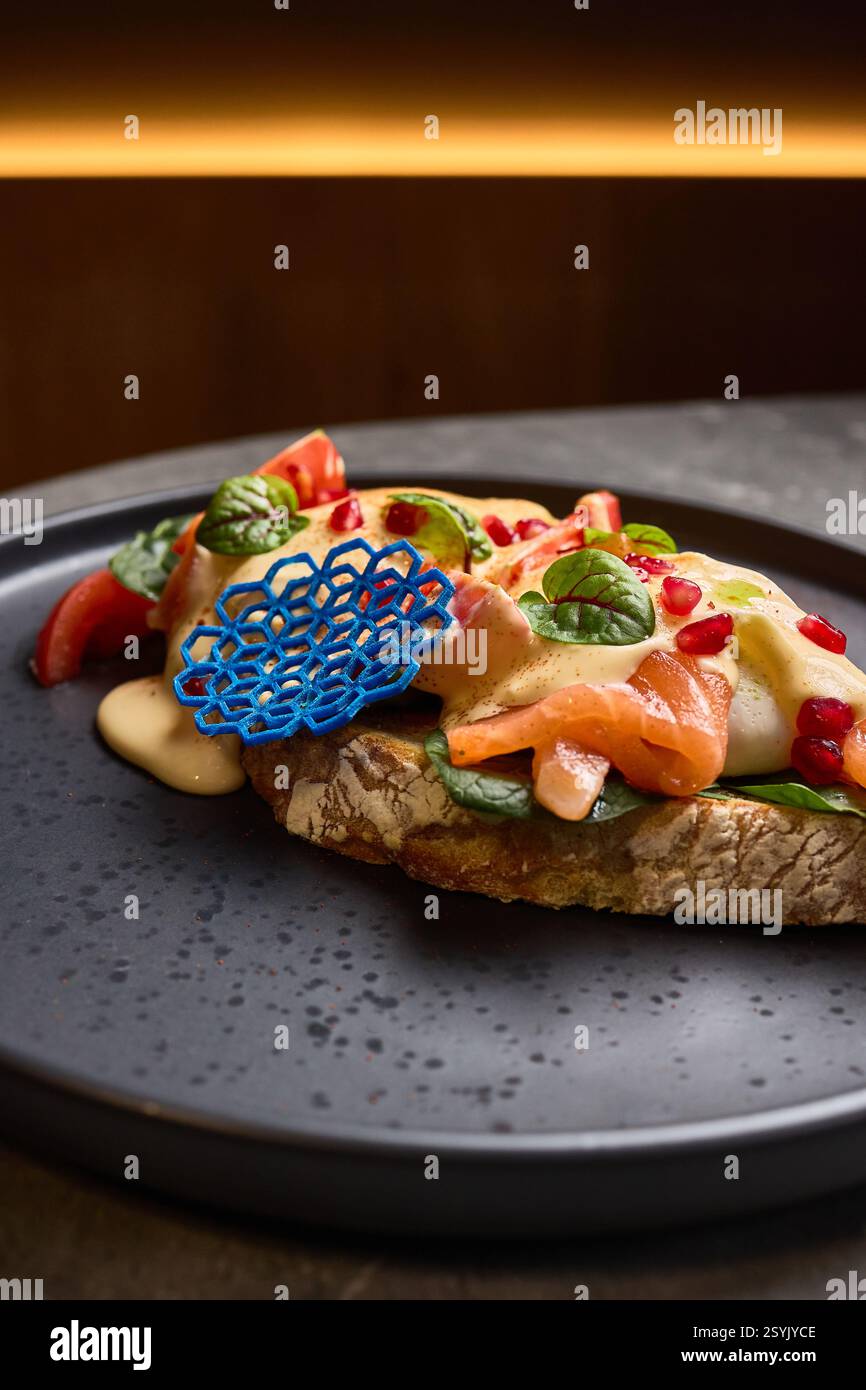 Sandwich di salmone a vista con condimenti colorati su piatto scuro, presentazione gourmet con elementi ornati, concetto di stile alimentare Foto Stock