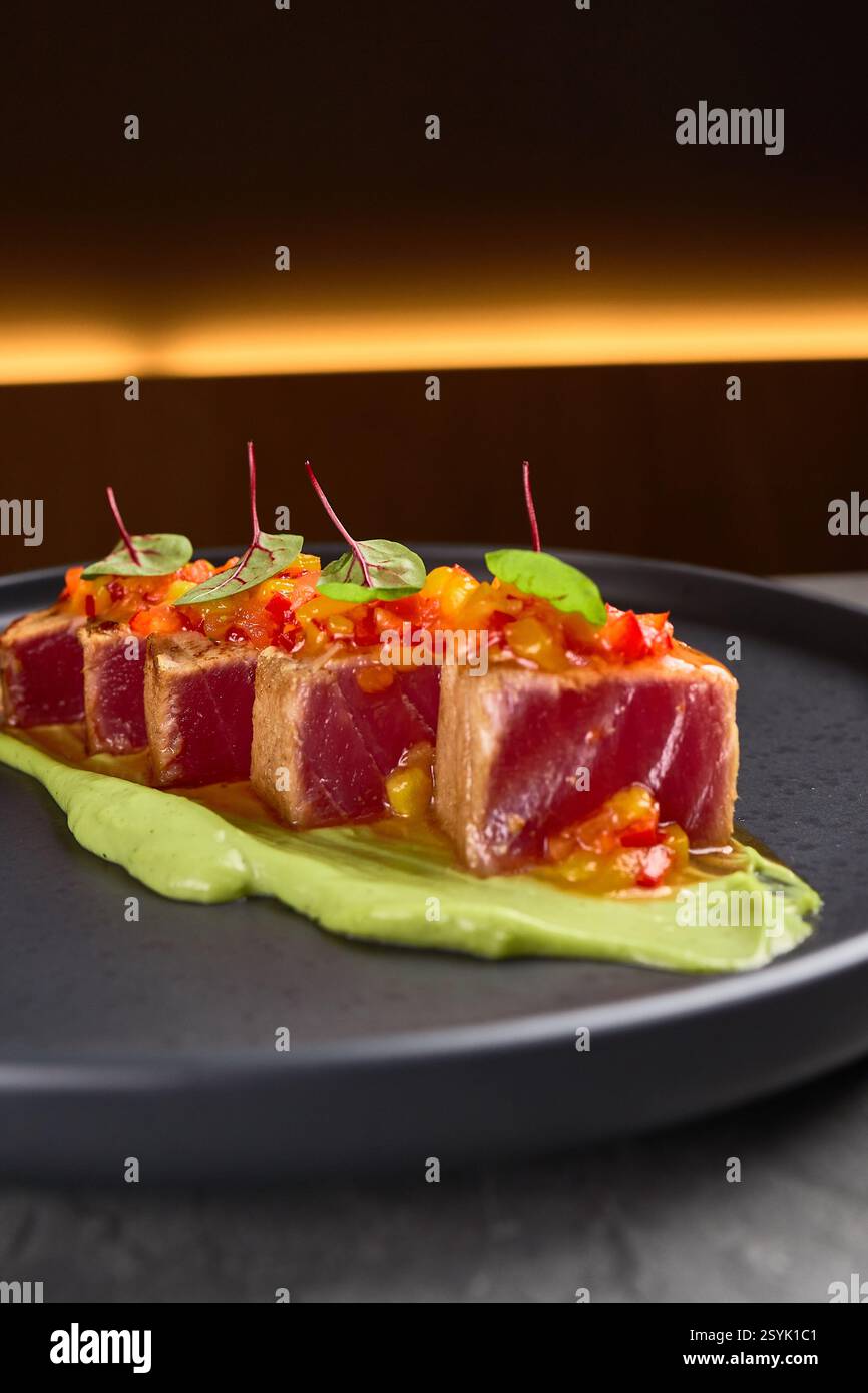 Purea di avocado e microgreen con fette di tonno scottate su un piatto nero che incarna il concetto di presentazione gastronomica Foto Stock