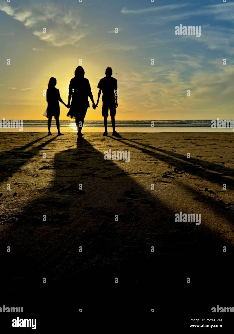 Silhouette di una famiglia di tre persone che camminano sulla spiaggia al tramonto con lunghe ombre. - Immagine stock catturata con smartphone