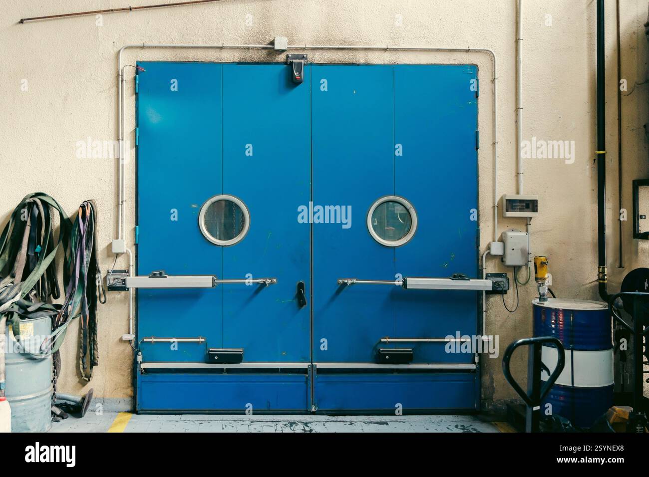 Grandi porte doppie blu con finestre rotonde in ambiente industriale, dotate di meccanismi di sicurezza e rinforzi in metallo Foto Stock