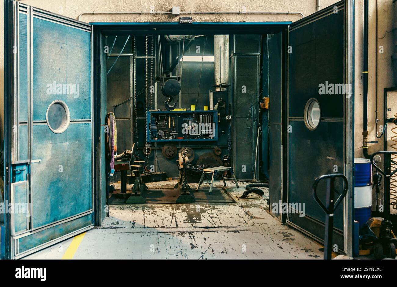 Grandi porte industriali blu si aprono per rivelare uno spazio interno con apparecchiature, cavi e strutture metalliche in fabbrica. Foto Stock